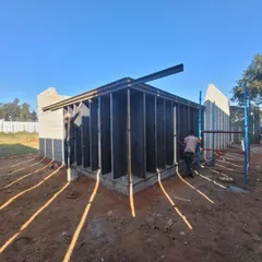 Workers install the structural framework of the gallery. The morning light casts long shadows, highlighting the rhythm of the vertical fins that will define the building's facade.