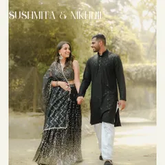 An elegant shot of a couple in coordinated black traditional outfits, walking hand-in-hand through a park, capturing a moment of happy connection.