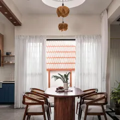 This dining area is defined by a double-height cutout in the ceiling, allowing natural light to flood the space. A cluster of pendant lights hangs through the opening, connecting the ground floor to the level above and creating a dramatic focal point.