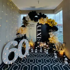 A sophisticated and stylish setup for a 60th birthday celebration. We used a black, white, and gold color palette, a balloon arch, and large marquee numbers to create a chic and celebratory photo corner.