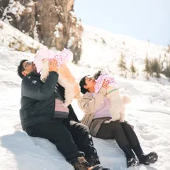 A heartwarming family portrait in the snow, with a couple joyfully lifting their two tiny Shih Tzu babies.