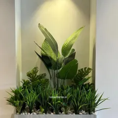 A modern, minimalist planter box filled with a curated selection of artificial grasses and large-leaf plants, perfectly fitting into an illuminated wall niche.