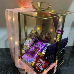 The metal bow hamper is all about elegance. Its sleek black base and gold metal frame, wrapped in soft tulle, create a luxurious presentation for chocolates or fragrances.