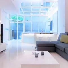 A wide shot of the living room, showing the open-concept layout that connects to the kitchen and an outdoor space. The polished white floors enhance the sense of space.
