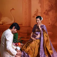 This shot captures a beautiful, traditional gesture of love and care. The husband-to-be attends to his wife's feet as she sits, adorned in a stunning silk saree.