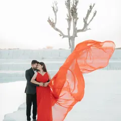 A bold and dramatic shot from a pre-wedding session at a mineral quarry. The vibrant red of the flowing gown against the stark white landscape creates a powerful, high-fashion image that tells a story of passionate love.