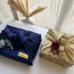 We love using Furoshiki, the Japanese art of fabric wrapping. This image showcases two different styles, one in royal blue and another in gold velvet, each adorned with floral details, offering a sustainable and stunning alternative to paper.