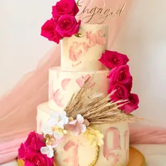 This three-tier engagement cake is a showstopper, featuring a textured pink buttercream effect and adorned with vibrant fresh magenta roses and dried wheat.
