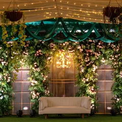 A lush green stage backdrop with a beautiful floral arrangement and an elegant chandelier, showcasing a classic and romantic decor theme.