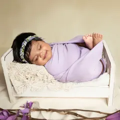 A blissful smile from a sleeping newborn, swaddled in soft lavender and resting in a miniature white crib. I use gentle colors and props to create a peaceful and beautiful scene.