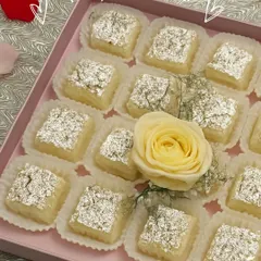 A beautiful box of our Nariyal ki Chakki, adorned with a fresh rose. This sweet is delicate, fragrant, and perfect for any celebration.