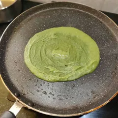 A vibrant green palak chilla (spinach crepe) cooking on a tawa. This is a nutritious and tasty breakfast dish.