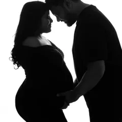 A dramatic and romantic silhouette of the couple. This black and white image captures their intimacy and the beautiful outline of the baby bump against a stark white background.