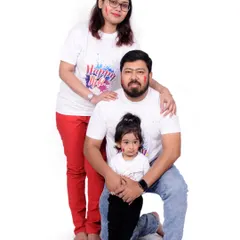 A full-length family portrait from a Holi photoshoot. The simple white outfits provide the perfect canvas for the bright colors, creating a classic festive memory.