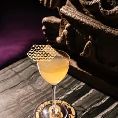 A close-up of a craft cocktail at Ocho Bandra, featuring a unique honeycomb-patterned garnish. The moody lighting and marble tabletop add to the sophisticated feel.