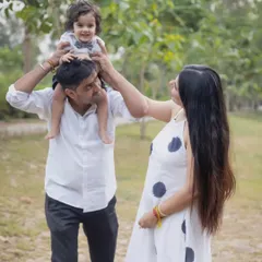 A playful and candid moment during an outdoor family photoshoot. The father has his toddler on his shoulders while the mother looks on lovingly, capturing the pure joy of family life.