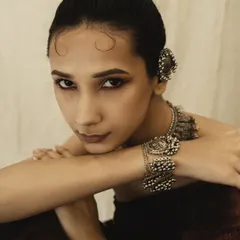 A close-up portrait that feels intimate and direct. The pose, with arms crossed, draws attention to the ornate bracelet and the model's compelling gaze.