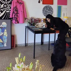 Our studio is a living gallery of our experiments and passions. Here I am at my workspace, surrounded by finished canvases, works-in-progress, and my ever-present supervisor, Kai.