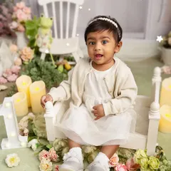 A little lady in her pastel world. This full-shot portrait shows a one-year-old girl in a lovely, soft-themed setup with flowers and candles, perfect for a first birthday.