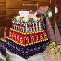 A multi-tiered chocolate tower made with Dairy Milk, KitKat, Ferrero Rocher, and Raffaello, topped with white roses. This is a stunning and delicious centerpiece for any celebration.