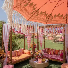 A cozy canopy seating area with gingham and striped cushions in shades of pink and orange. The custom-printed parasol adds a touch of Rajasthani flair.