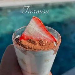 A perfect poolside treat. This is a close-up of my classic tiramisu served in a cup, dusted with cocoa powder and topped with a fresh strawberry slice.