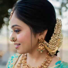 A side profile showing a classic South Indian bridal hairstyle. The hair is pulled back into a neat bun, adorned with fresh flowers and a traditional hair accessory.
