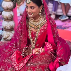 A candid moment from a North Indian wedding ceremony. The bride looks serene and beautiful in her red lehenga, with makeup that enhances her features without overpowering them.