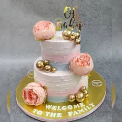 A beautiful two-tiered "Welcome to the Family" cake. This tri-color icing design is adorned with large peonies and gold spheres, making it an elegant choice for a baby shower.