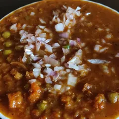 A close-up of my rich pav bhaji, a mash of fresh vegetables in a spiced tomato gravy, topped with finely chopped onions.