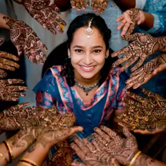 A creative and heartwarming Mehendi photo, with the bride's beautiful smile framed by the henna-adorned hands of her friends and family.