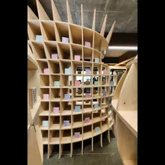 An interior view of the curved 'Stradata' folly, showing how the stacked layers of plywood create a dynamic, flowing space. The design plays with perspective and form, inviting people to walk through and experience its plasticity.