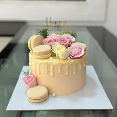 A lovely peach-colored drip cake topped with a beautiful arrangement of fresh pink and yellow roses, macarons, and delicate greenery.