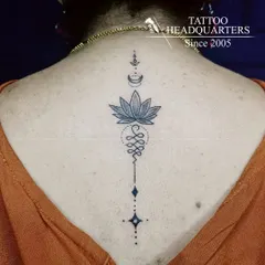A beautiful Unalome tattoo on the spine, symbolizing the path to enlightenment. The design incorporates a lotus flower, representing purity and spiritual awakening.