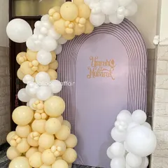 An elegant 'Umrah Mubarak' decoration to welcome loved ones. The setup features a lavender arched backdrop with a beautiful balloon garland in pastel yellow and white.