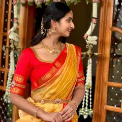 A client styled in a traditional half saree for a festive occasion. The bright red blouse features subtle kasu work on the sleeves, perfectly complementing her temple jewellery.