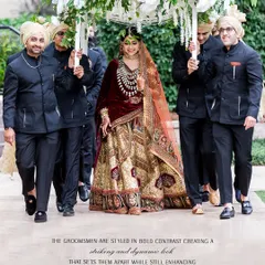 The bride's grand entrance, a moment of pure heritage and emotion. We styled her in a magnificent red and gold lehenga, rich with traditional embroidery. The groomsmen, dressed in contrasting black bandhgalas, create a striking and dynamic frame, enhancing the bride's regal presence.