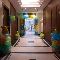 An entrance to a jungle-themed party in a hotel corridor. A colorful balloon arch and giraffe-themed balloon pillars welcome guests to the celebration.