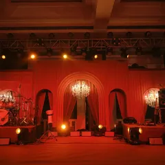 The stage for the evening's entertainment, washed in a warm red glow. The arched backdrop and crystal chandeliers add a touch of classic elegance to the modern monochromatic theme.