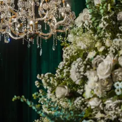 A close-up of a chandelier and a large white floral arrangement. The warm light from the chandelier beautifully illuminates the flowers, making them glow.