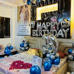 A closer look at the birthday setup, highlighting the details like the balloon teddy bears on the side tables and the heart-shaped rose petal arrangement on the bed.