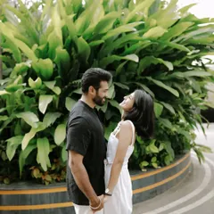 A happy, candid moment between a couple in casual attire, holding hands against a backdrop of green foliage.