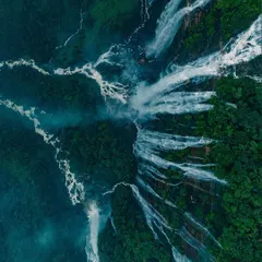 A dramatic top-down drone shot of waterfalls in Meghalaya, showing the raw power of water as it carves through the dense green forest.