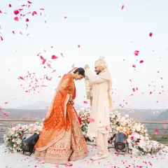 A shower of rose petals rains down on the couple during their varmala exchange. This beautiful, candid moment is full of color, emotion, and celebration.