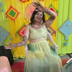 A happy client posing during her Haldi ceremony. Her full-arm traditional mehandi looks beautiful with her festive attire and colorful background.