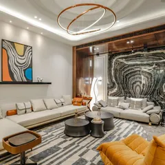 This contemporary living room at our Vikaspuri project features a bold, book-matched marble wall that acts as a piece of natural art. The space is furnished with a large sectional sofa, a unique orange lounge chair, and a geometric-patterned rug.