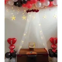 For a truly romantic gesture, I can create an intimate canopy setup in your room. This one includes a sheer curtain with fairy lights, a ceiling garland of red and black balloons, and special 'I love you' heart-shaped foil balloons.