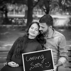 A classic black and white photo of an expecting couple on a park bench. The "Coming Soon" sign adds a sweet sense of anticipation to this peaceful moment.