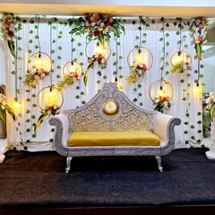 An elegant reception stage design with a classic white and gold loveseat. The backdrop features hanging floral hoops with vintage style bulbs, creating a warm and romantic ambiance.
