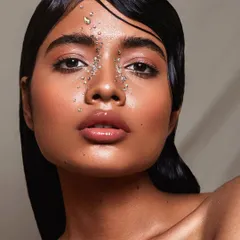 A direct and impactful beauty portrait with under-eye crystal embellishments. The focus is on the model's flawless skin and the striking, symmetrical makeup detail.